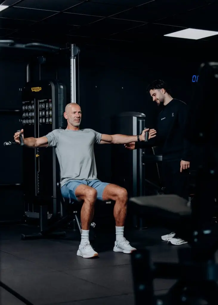 Coach begeleidt krachttraining op de chest press machine