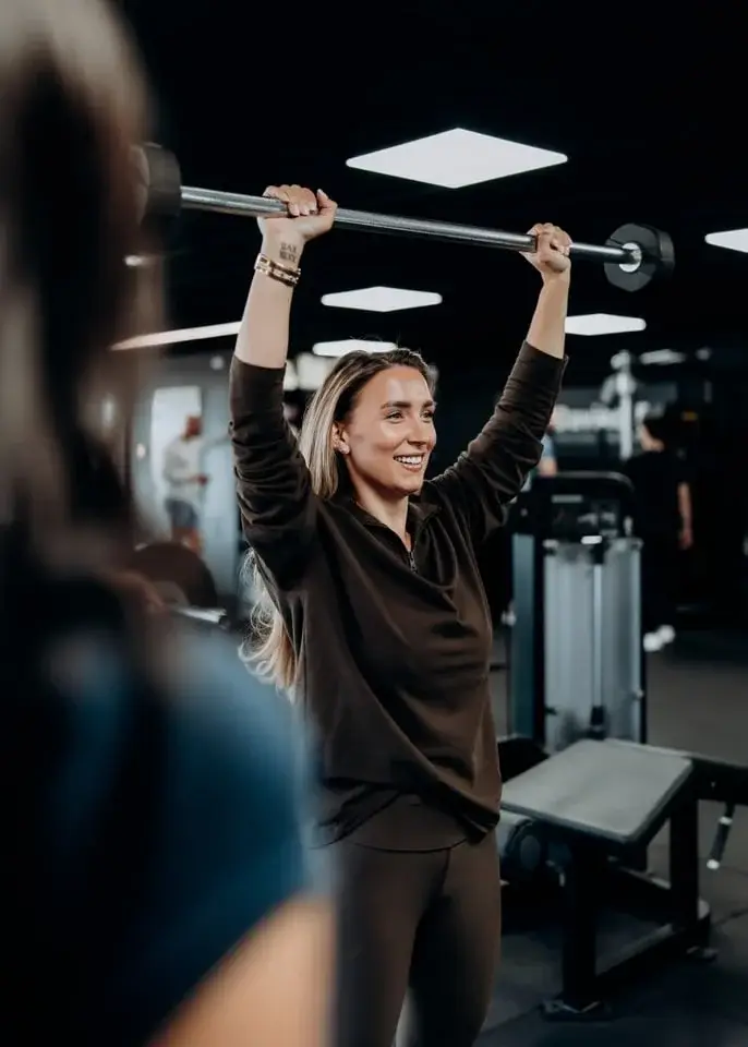 Vrouw doet een overhead press met halterstang in de gym